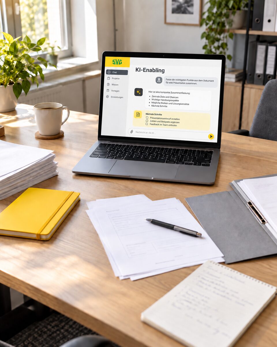 Arbeitsplatz mit aufgeklapptem Laptop und geöffnetem KI-Fenster, daneben Papierstapel, Ordner und ein gelbes Notizbuch